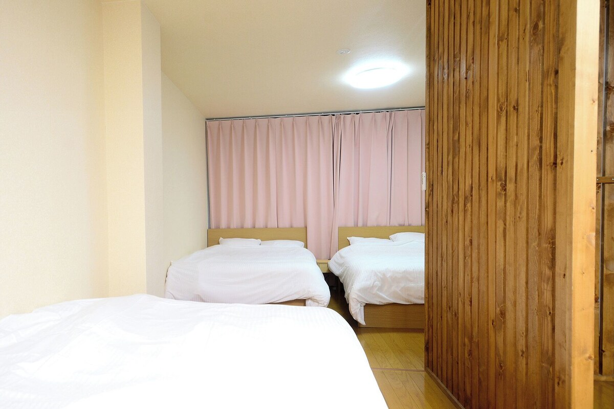 Quarto com duas camas, lambris de madeira em uma parede e uma cortina na janela.