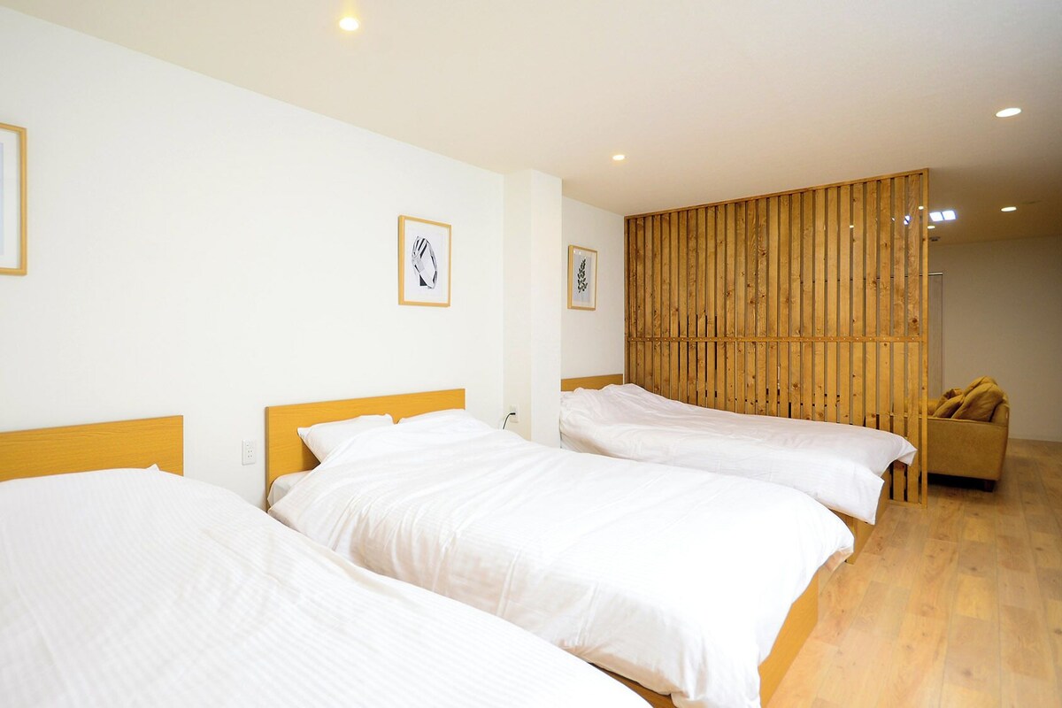 Quarto de hotel com três camas de solteiro, uma divisória de madeira e um sofá.