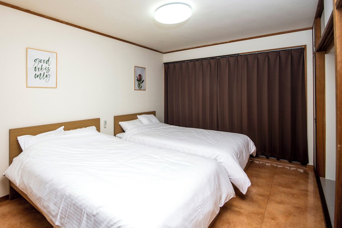 Quarto com duas camas, luminária no teto, quadro pendurado na parede e janela com cortinas.