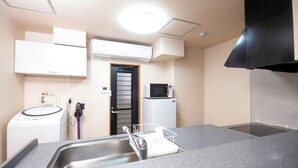 A compact kitchen with a built-in microwave, a refrigerator, a washing machine, and a sink with a dish rack. - K's Hotel (Takamatsu)
