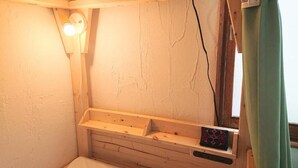 A small, dimly lit room with a wooden bench, a wall-mounted light fixture, and a window with a curtain.