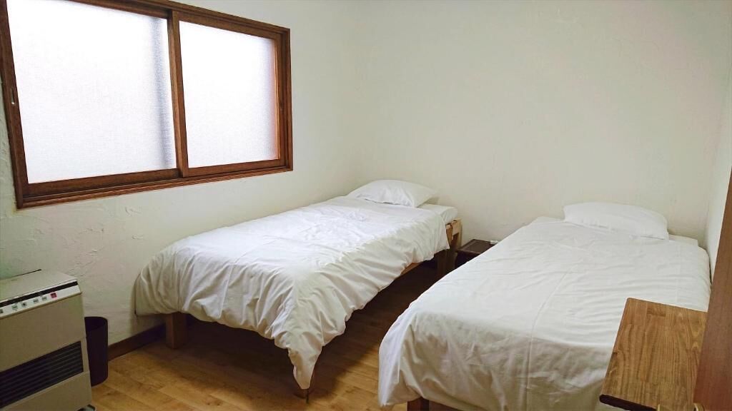 A small room with two single beds, a wooden floor, a window, and a heater.