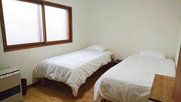 A small room with two single beds, a wooden floor, a window, and a heater.