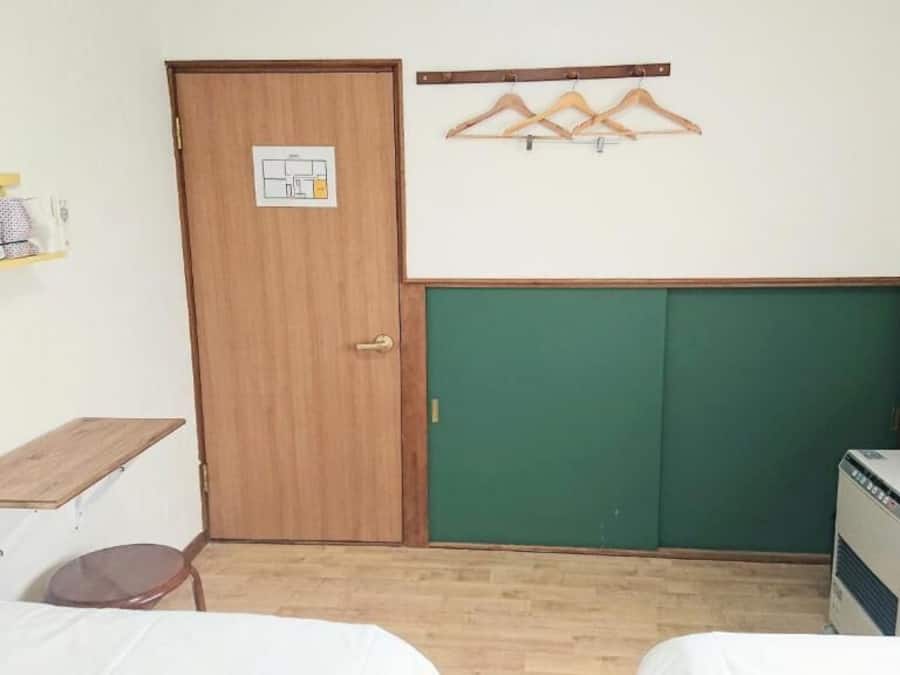 A room with a wooden door, a green chalkboard, a desk with a chair, and a small heater.