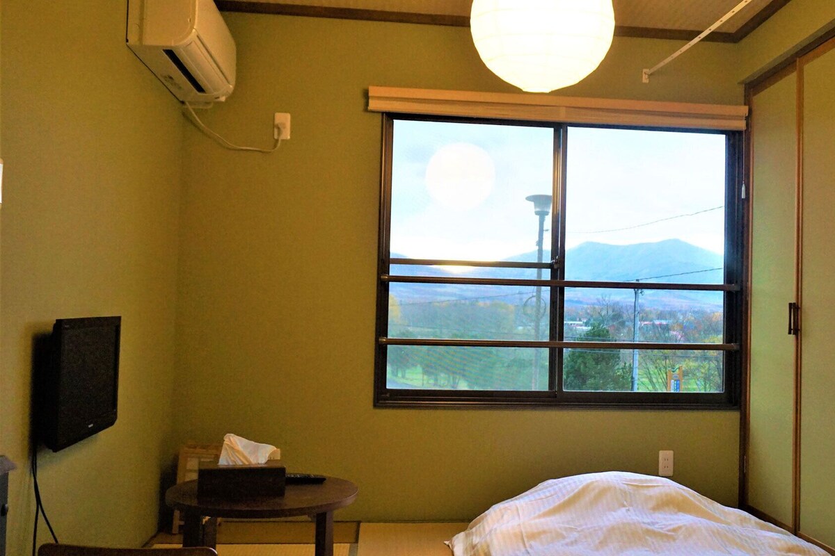 Una habitación con cama, una mesita, televisión y un ventanal con vistas a montañas.