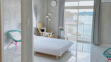 Ein modernes Hotelzimmer mit einem großen Bett, einem Sessel, einem kleinen Tisch und Meerblick.