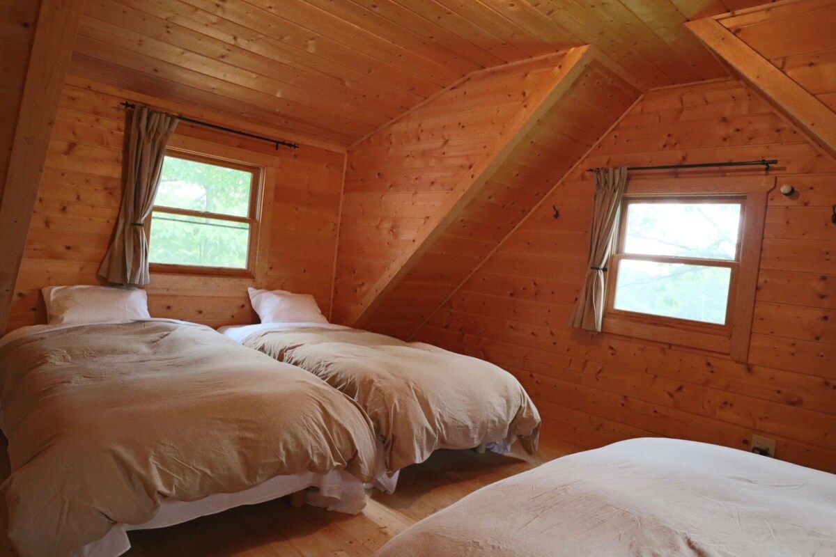 A wooden cabin room with two beds, two windows, and a sloped ceiling.