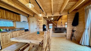 A wooden interior with a dining table, benches, a kitchen area, and a living space. - Place Yatsugatake Oigamori Cottage (Hokuto)