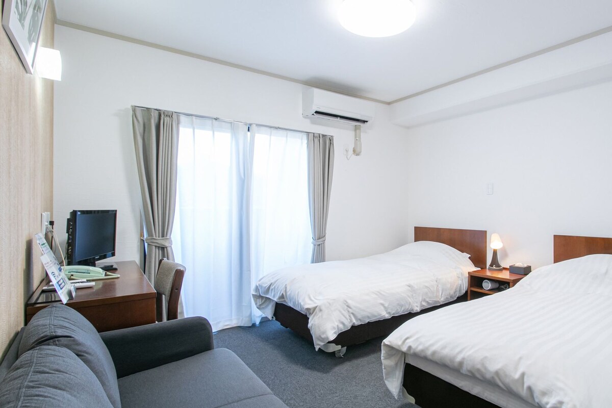 Habitación de hotel con dos camas, un escritorio con computadora y una silla.