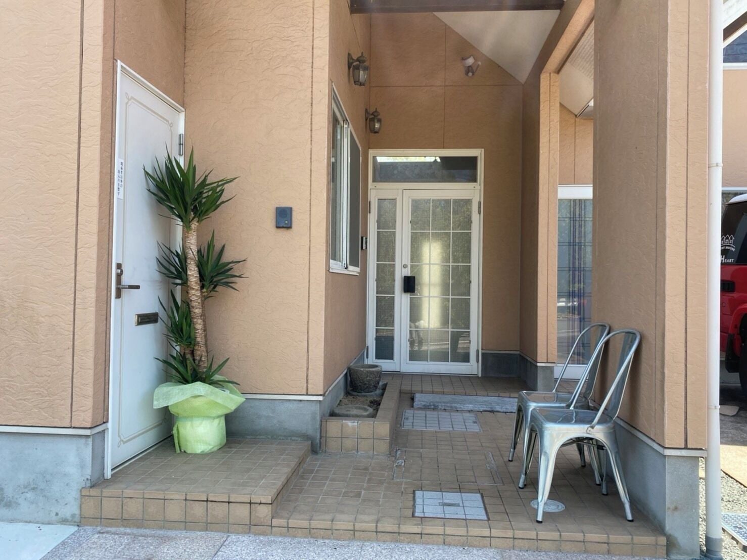 A building entrance with a door, a potted plant, and metal chairs outside.