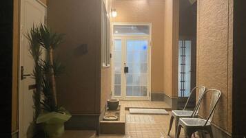 A hallway with a door leading to a room, a potted plant, and two chairs.