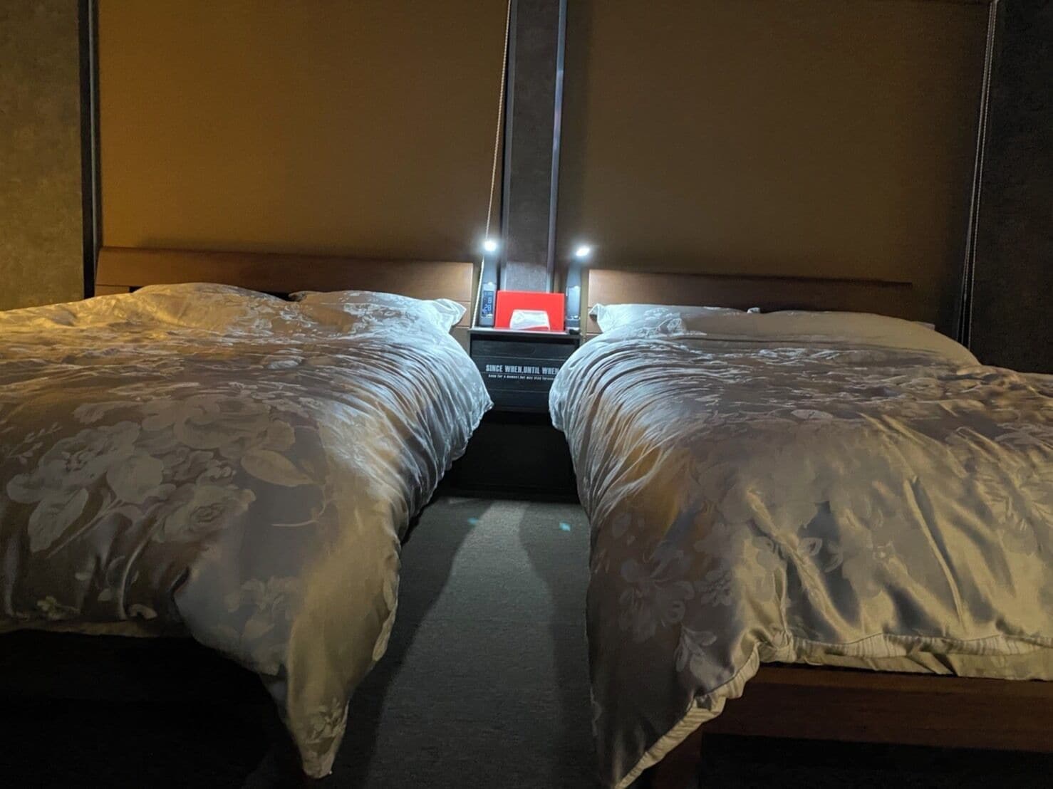 Habitación de hotel con dos camas, una mesita de noche y un objeto rojo sobre ella.