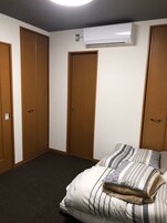 Un dormitorio con cama, almohadas a rayas, suelo alfombrado, armario de madera y un equipo de aire acondicionado.