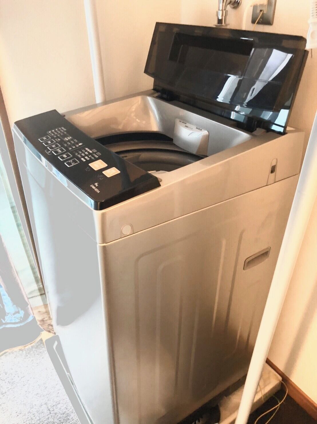 Una unidad compacta de lavadora y secadora de acero inoxidable con panel de control digital, ubicada en un rincón con un picaporte visible.