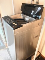 Una unidad compacta de lavadora y secadora de acero inoxidable con panel de control digital, ubicada en un rincón con un picaporte visible.