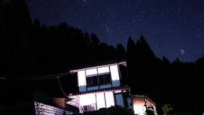 Una casa moderna amb una finestra gran, envoltada d'arbres sota un cel ple d'estrelles.