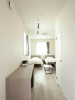 Un pasillo estrecho que da a un dormitorio con dos camas, un escritorio y una ventana con cortinas.