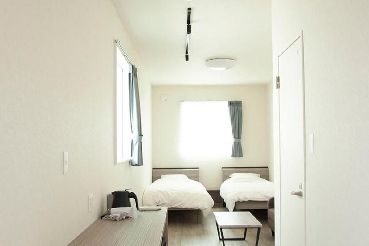 Un pasillo estrecho que da a un dormitorio con dos camas, un escritorio y una ventana con cortinas.