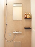 Un baño con ducha, espejo y tres botellas de artículos de tocador en un estante.