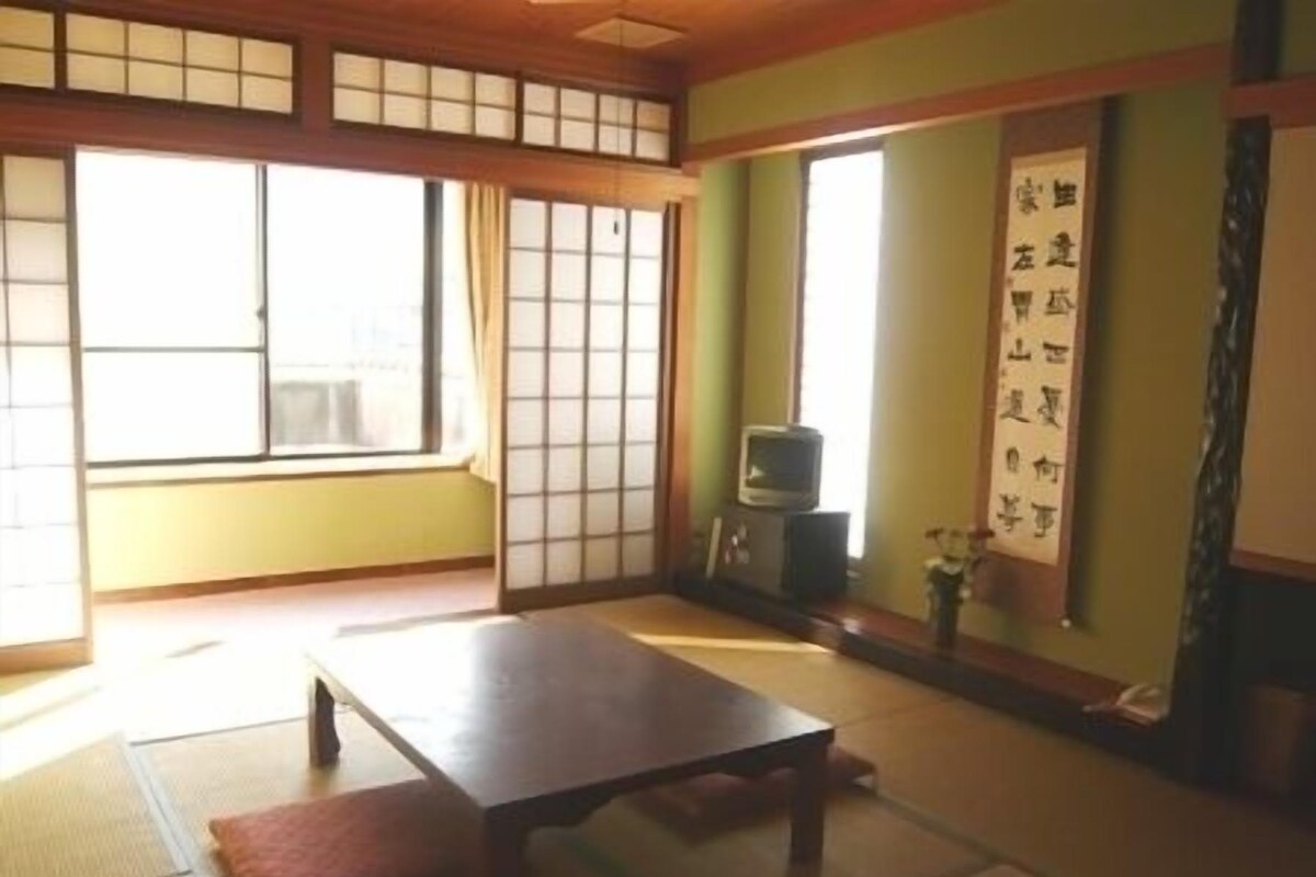 Una habitación japonesa tradicional con suelo de tatami, una mesa baja, puertas correderas y un televisor.