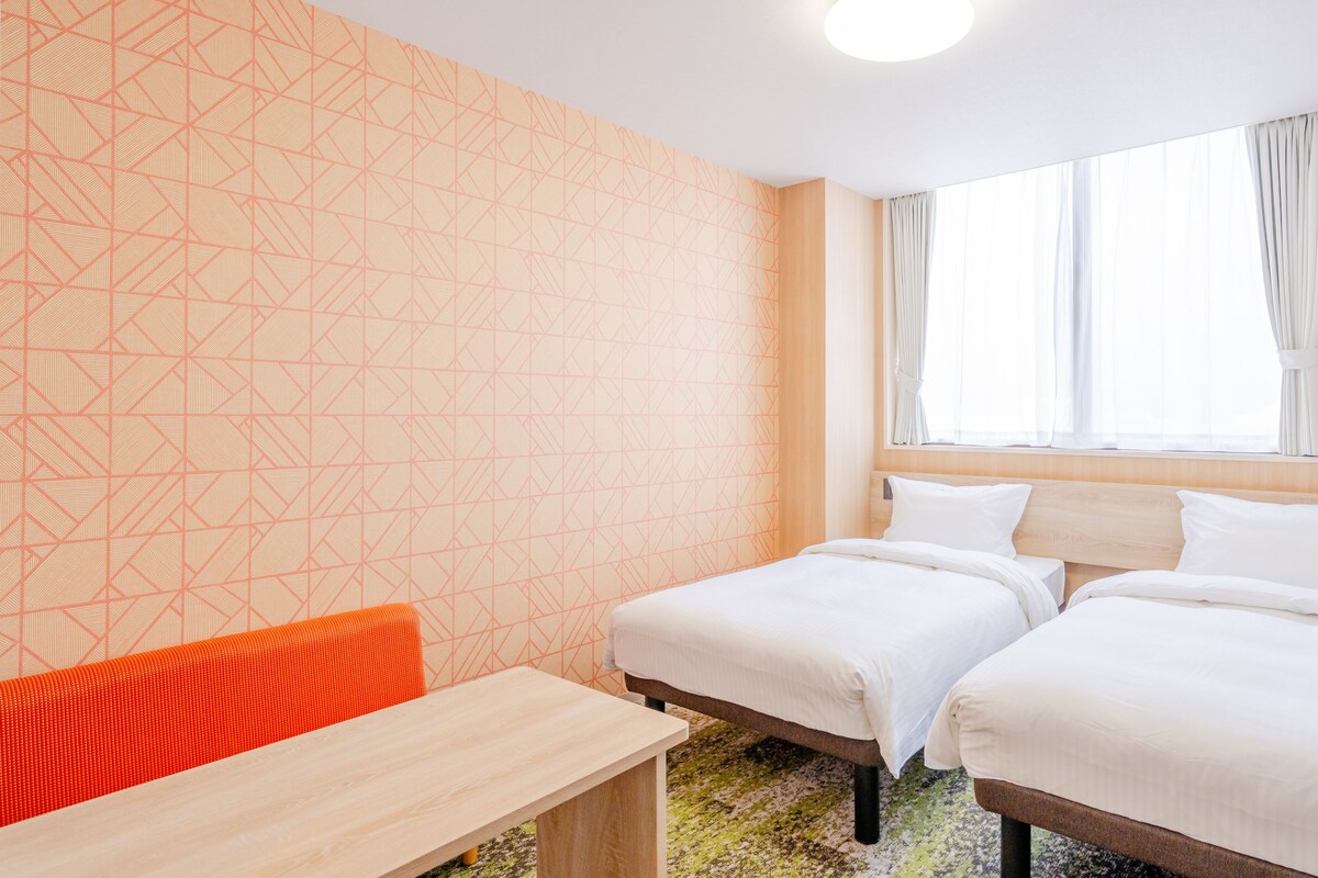 Habitación de hotel con dos camas, un escritorio y una ventana con cortinas.