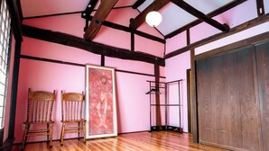 A room with wooden flooring, a large framed painting, two chairs, a metal rack, and a wardrobe. - Idemaru Guest House (Ueda)
