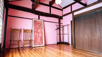 A room with wooden flooring, a large framed painting, two chairs, a metal rack, and a wardrobe.