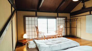 A traditional Japanese room with tatami flooring, a low wooden bed, a table with chairs, and a sliding door.