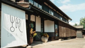 A traditional building with a sign reading 'HOSTELS/SALON' and a large potted plant in front. - Idemaru Guest House (Ueda)