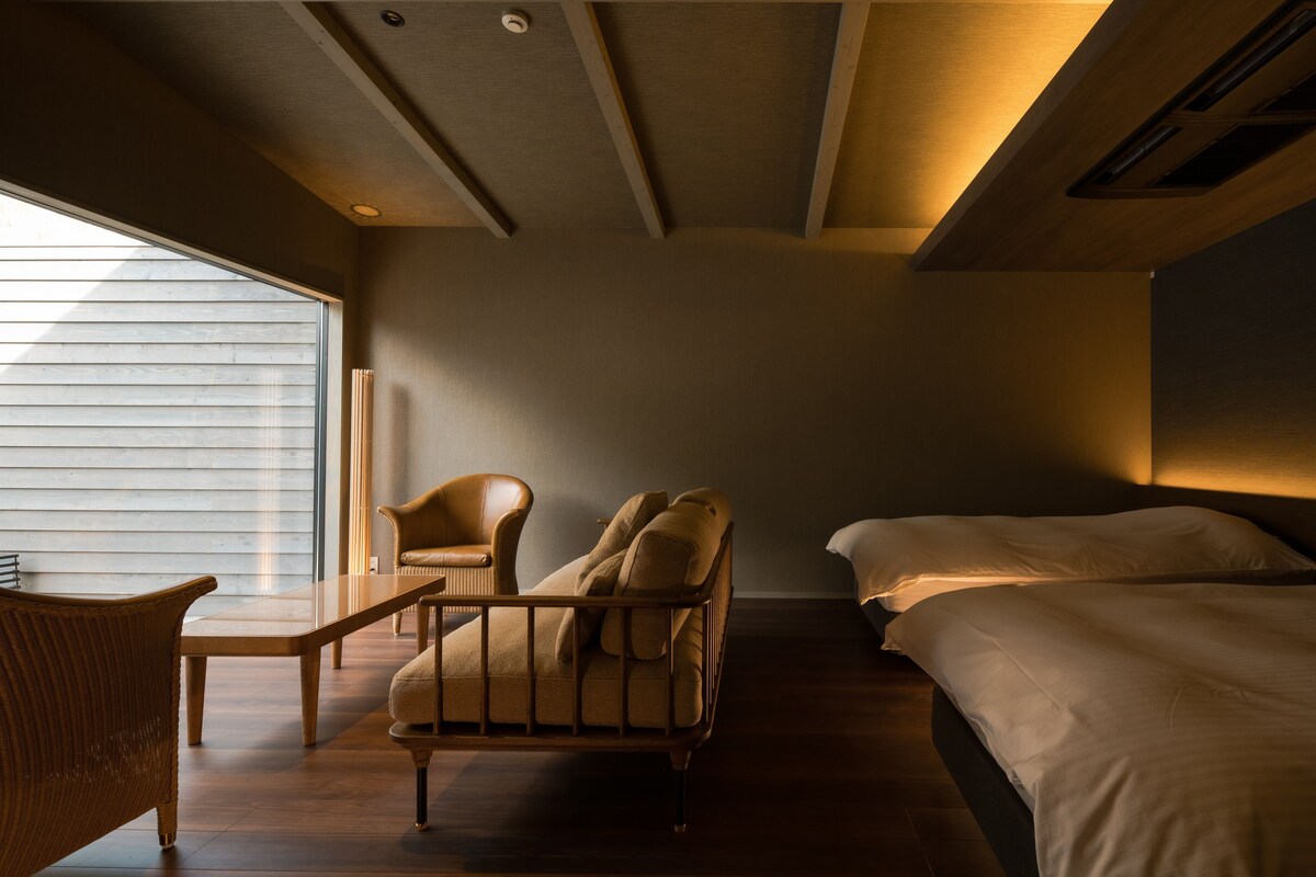 Una habitación con cama, silla, mesa y ventana.