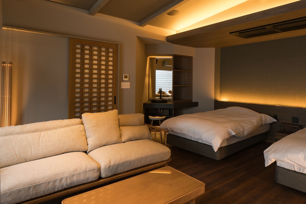 Habitación de hotel con sofá, dos camas, una mesita, un espejo y un panel de madera.