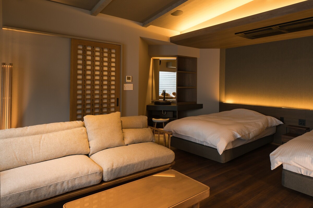 Een hotelkamer met een bank, twee bedden, een kleine tafel, een spiegel en een houten roomdivider.