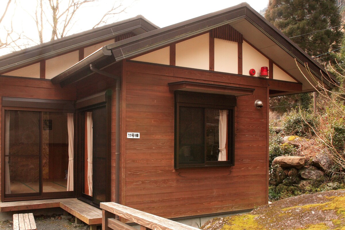 Una cabaña de madera con un amplio ventanal corredero, un porche pequeño y una ventana con cortina.