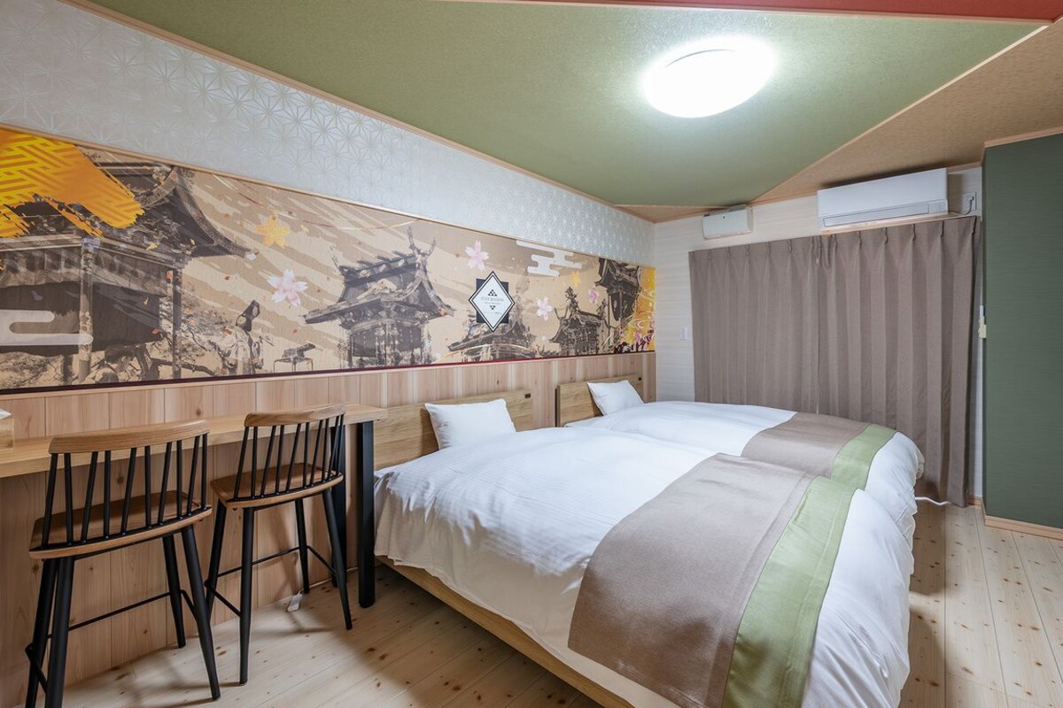 Hotelkamer met een bed, een bureau met twee stoelen, een wanddecoratie en een airconditioner.