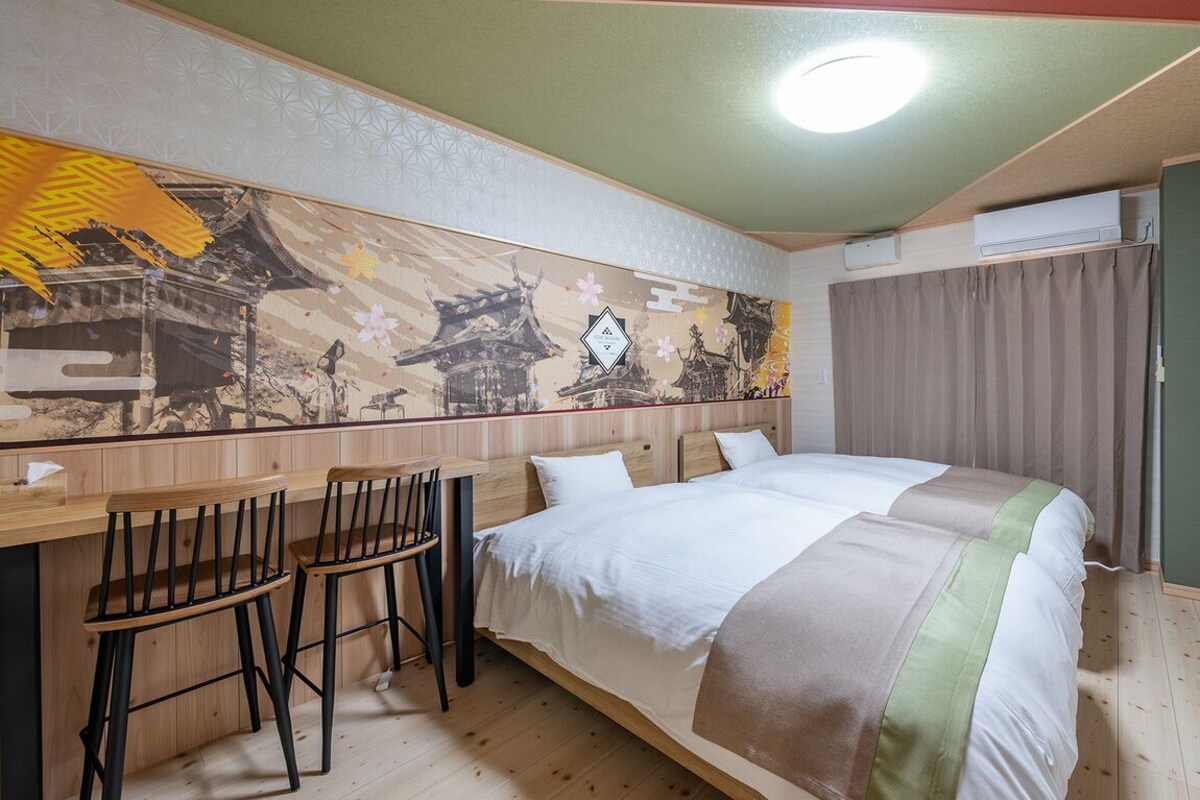 A hotel room with a bed, a desk with two chairs, a wall mural, and an air conditioning unit.