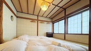 Una habitación tradicional japonesa con suelo de tatami, una cama grande con ropa blanca, un farol colgante y una ventana con diseño de cuadrícula.