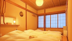 Una habitación tradicional japonesa con suelo de tatami, una cama grande con ropa blanca, techo de madera y ventana con diseño de cuadrícula.