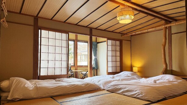 Una habitación japonesa tradicional con suelo de tatami, futón, puertas correderas shoji y una linterna colgante.