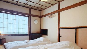 Una habitación de hotel con dos camas, un ventanal amplio, un reloj de pared y un televisor.