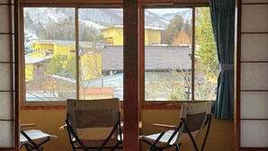 Una habitación con un ventanal grande, dos sillas plegables y una cama.