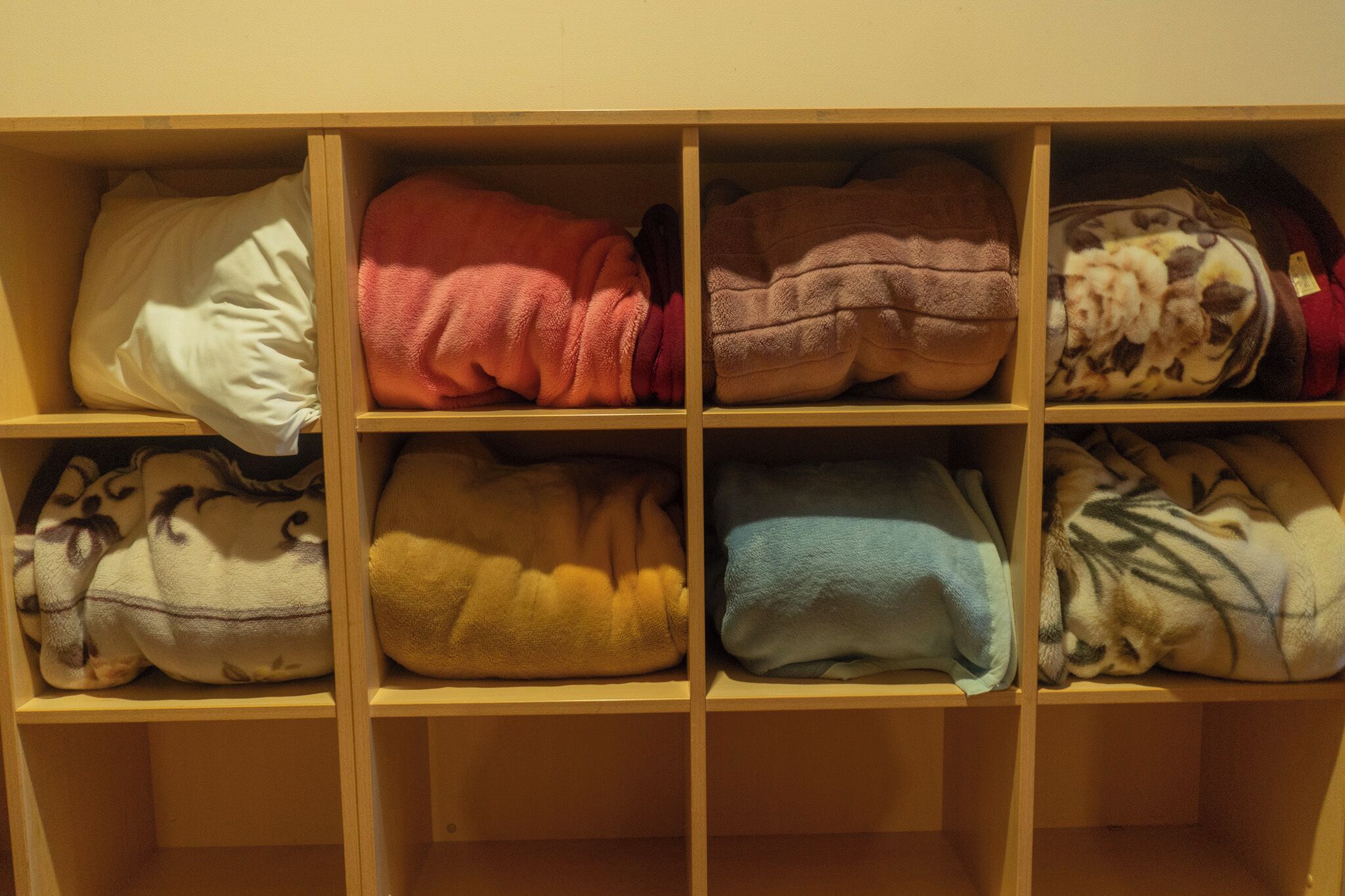 A wooden shelf with folded blankets in various colors.