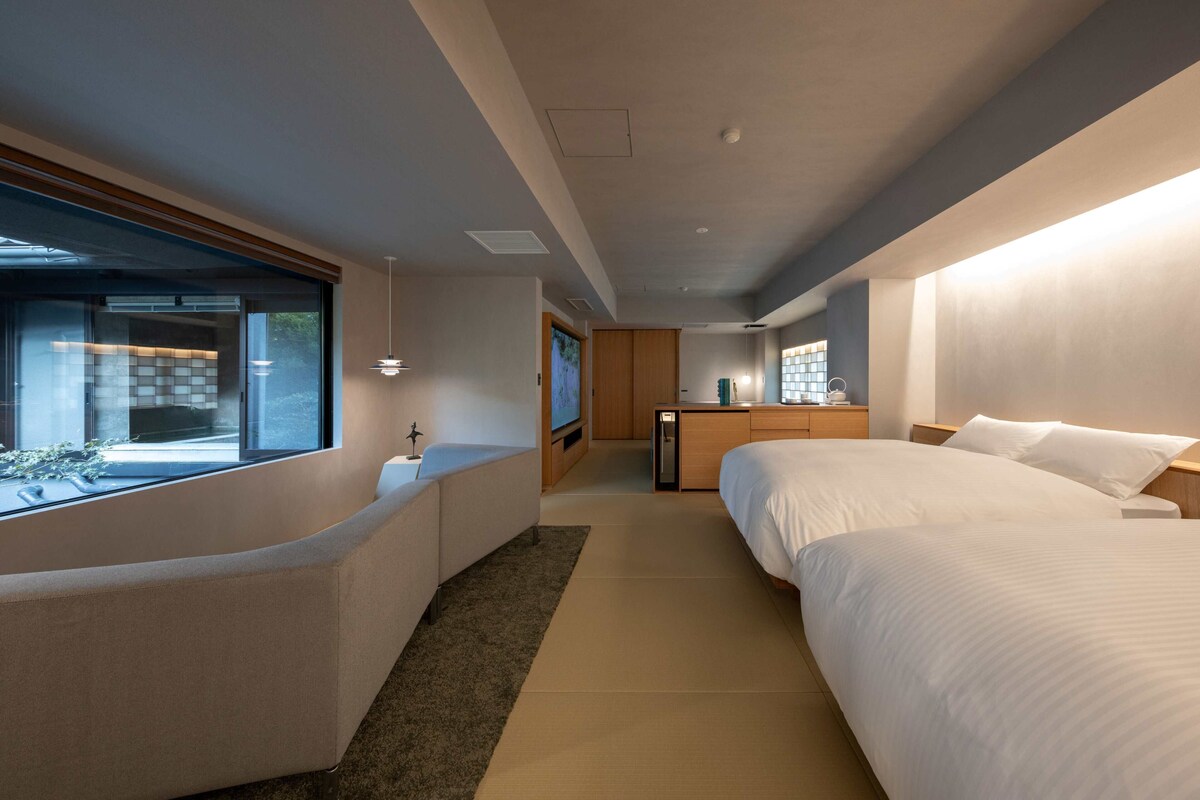 Quarto de hotel moderno com uma cama grande, um sofá, uma TV e uma escrivaninha.