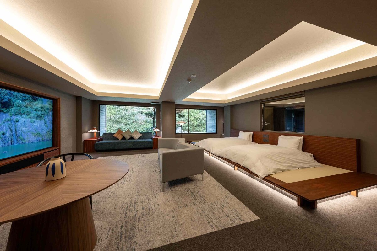 Quarto de hotel moderno com uma cama grande, um sofá, uma TV e uma mesa de jantar.