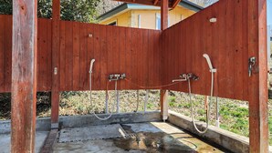 Ducha exterior de madera con dos cabezales y mangueras.