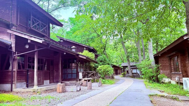 A rustic wooden cabin with a porch, surrounded by lush greenery and trees. - Akiu Kinoie Lodge Village (Sendai)