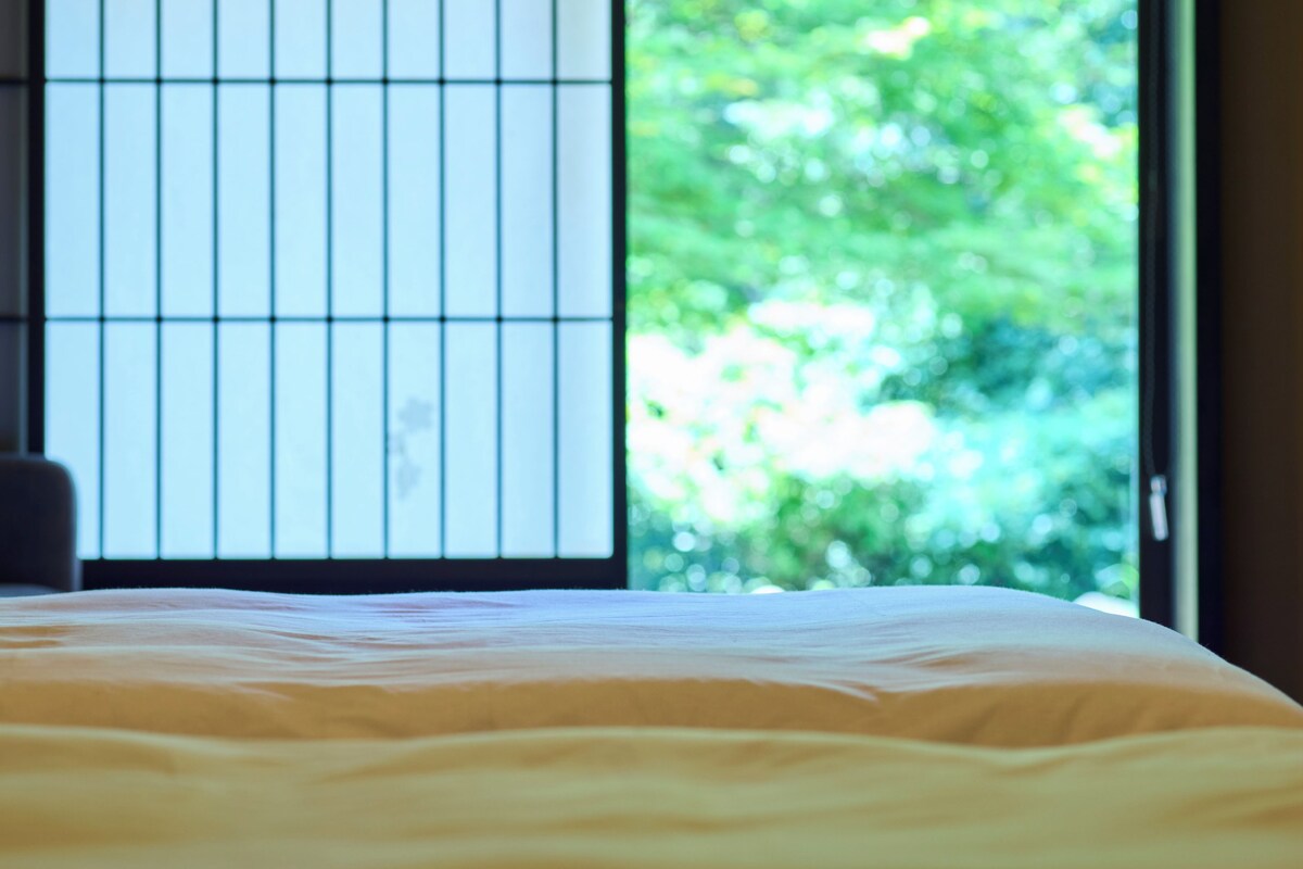 Een bed met een wit laken in een kamer met een groot raam.