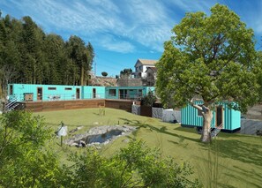 A turquoise building with a patio area, a small pond, and a tree. - The W Relax Garden Resort (Maebashi)