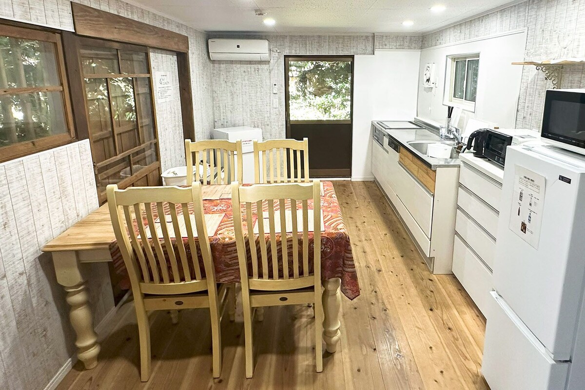 Een kleine keuken met een eettafel, stoelen, een magnetron en een koelkast.