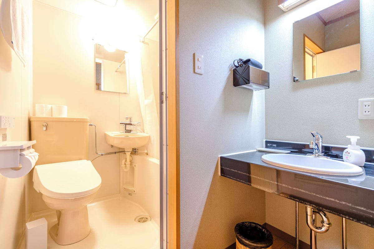 Un baño con inodoro, lavamanos, espejo y cubo de basura.