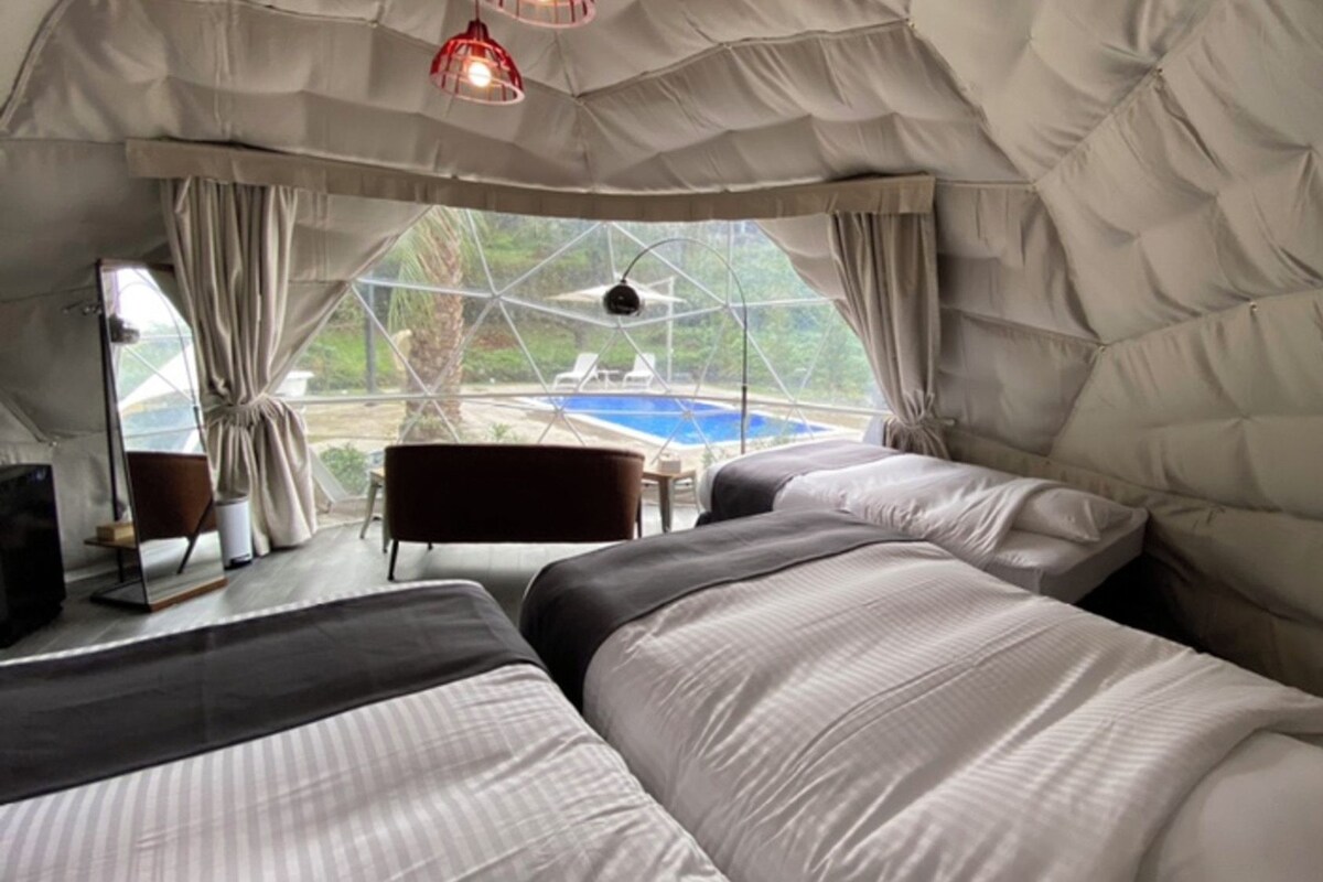 A tent-style room with two beds, a table, and a view of an outdoor swimming pool.